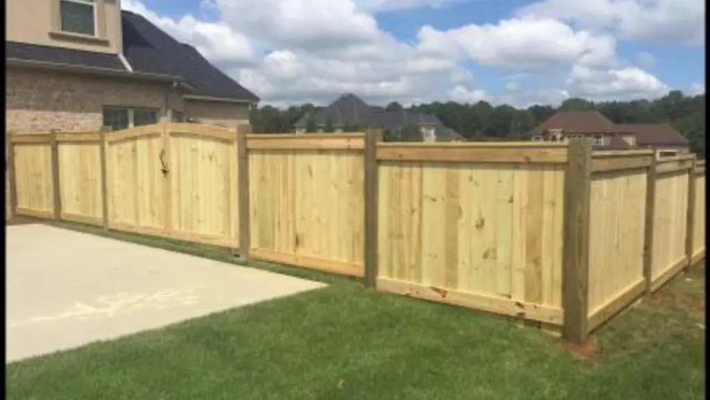 Board on board wood privacy fence with arched top panels and post caps beside a brick home in Warner Robins