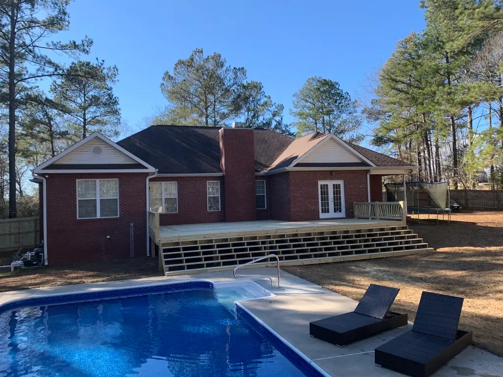Newly built timber deck with steps on a brick ranch home beside an inground pool